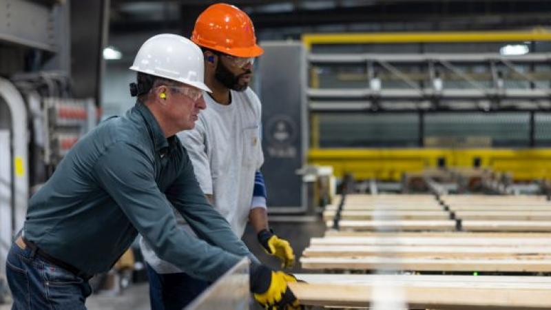 2 men one in white hat and other in orange shown working in a manufacturing unit wearing hard hat